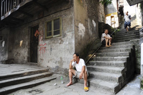 04.08.2012, Chongqing, China, Asia, Men sit on the steps in front of an old house in the old town of Shibati, on whose wall red letters inform the residents about the imminent demolition of the building to make room for new buildings, Asia