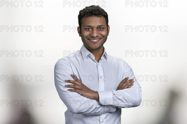 Handsome smiling man with crossed arms looking at camera. Portrait of indian businessman on blurred background