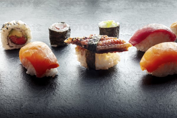 Sushi on a black slate plate. Nigiri with eel, salmon and tuna, roll with avocado and maki with cucumber on a black background, Japanese food on a plate at an Asian restaurant, Food photography, Food photography
