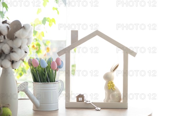 Key and tiny house of cozy home with Easter decor with rabbit and eggs on table of kitchen. Building, design, project, moving to new house, mortgage, insurance, rent and purchase real estate