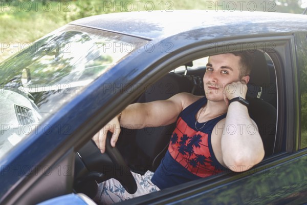 Portrait of smiling young man sitting in a car and looking at the camera on a sunny day