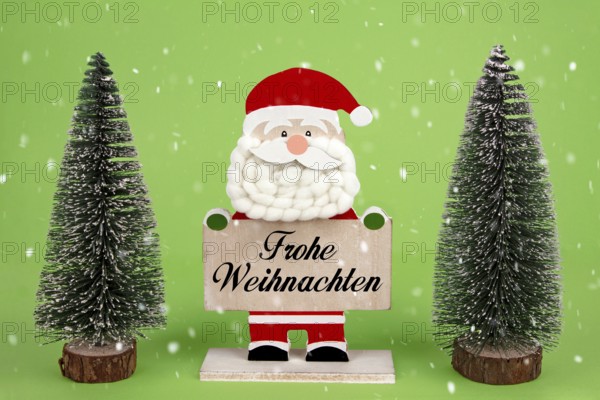 Dekorative hölzerne Santa Clause hält eine Tafel mit deutschem Text -Frohe Weihnachten- bedeutet Frohe Weihnachten