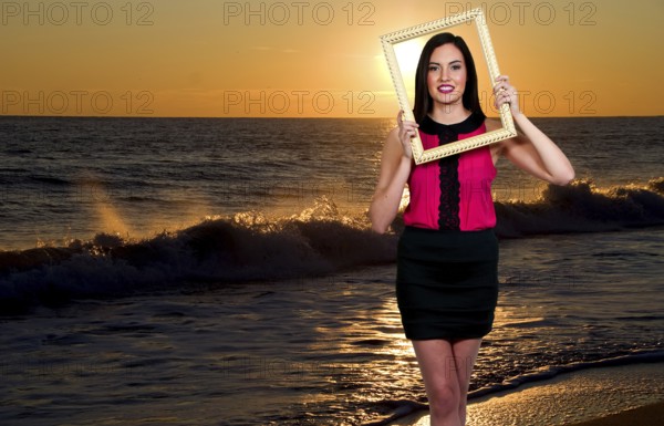 Beautiful woman looking through an ornate picture frame at the beach