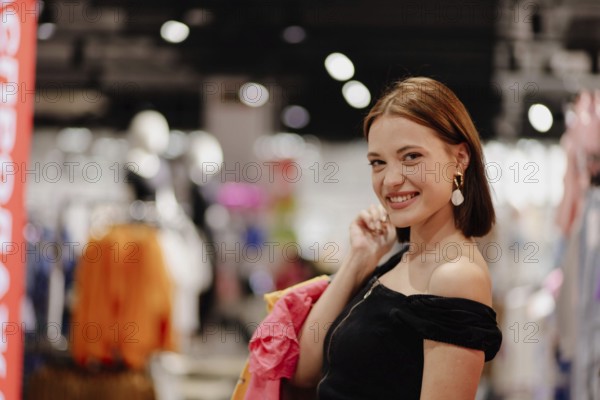 Happy woman shopping with colorful clothing behind her, smiling