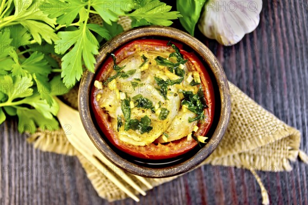 Fish baked in tomato in Zandvoort in clay bowl on a napkin of burlap, parsley on a dark wooden board on top