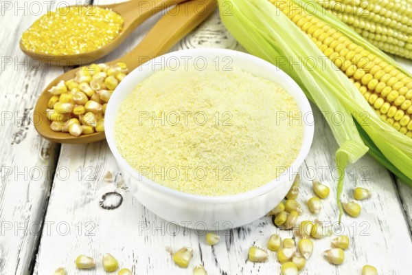 Flour corn in a bowl, groats and grain maize in the spoons, cobs on the background of wooden boards