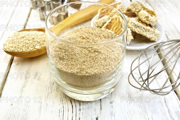 Sesame flour in a glass, a spoon with sesame seeds, cookie cutters and a mixer, biscuit on the background light wooden boards
