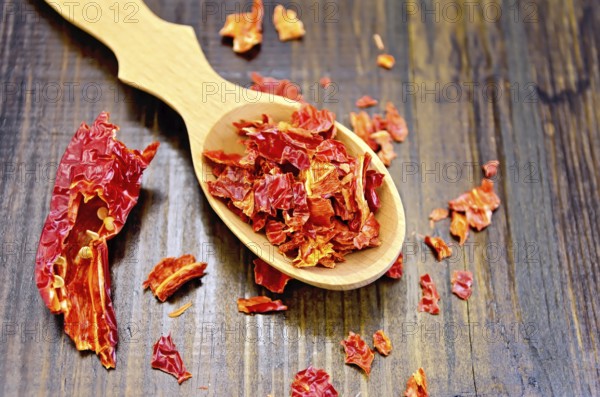 Red pepper flakes in a wooden spoon and a pod of dry red pepper on a wooden board