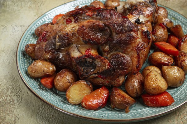 Pork knuckle baked with vegetables, new potatoes, on a plate, homemade, no people