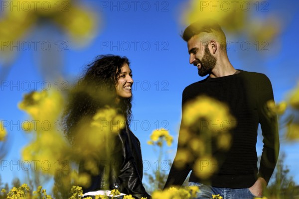 Portrait of a happy couple smiling holding hands looking at each other in a field of flowers in springtime