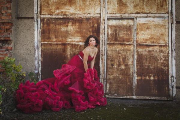 Woman in cloudy red dress is posing over rust wall. Fashion portrait without retouch, only make up