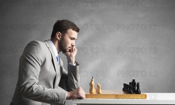Businessman moving chess figure in chessboard. Successful management and leadership. Handsome man in business suit at desk with chess on grey wall background. Operative tactics and strategy planning