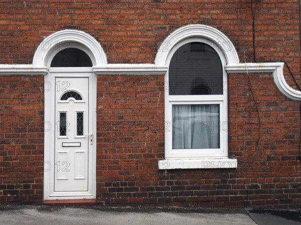 White front door and window of a typical old brick british terraced house with white decorative paintwork