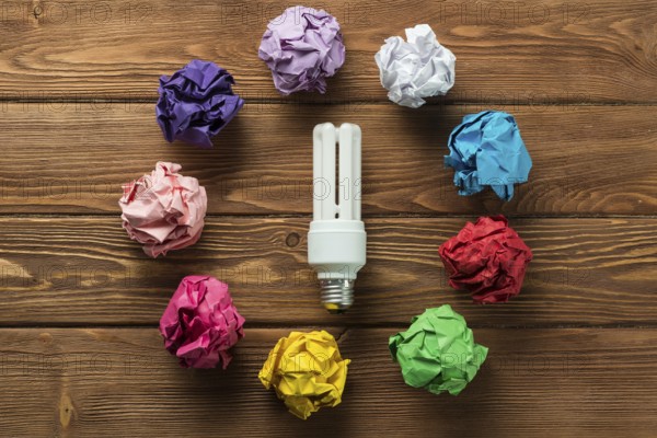 Lightbulb placed in circle of multiple crumpled paper balls on wooden table as means of searching of new ideas