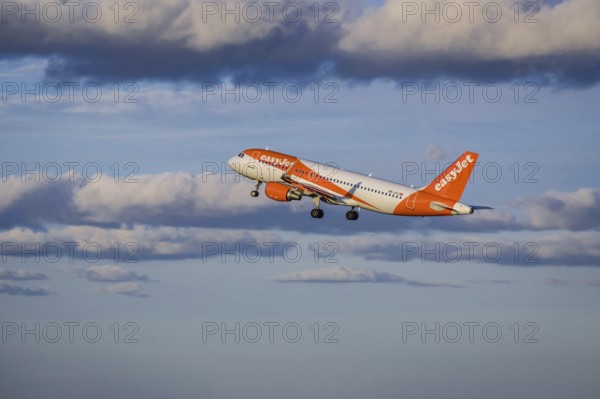 Lisbon, Portugal - Apr 29, 2024: EasyJet Airbus 320 aircraft shot mid-flight, ascending into clear blue sky with some clouds after takeoff on sunny day. Air traffic, vacations, travel, destinations, aircraft, low-cost airline, commercial flight