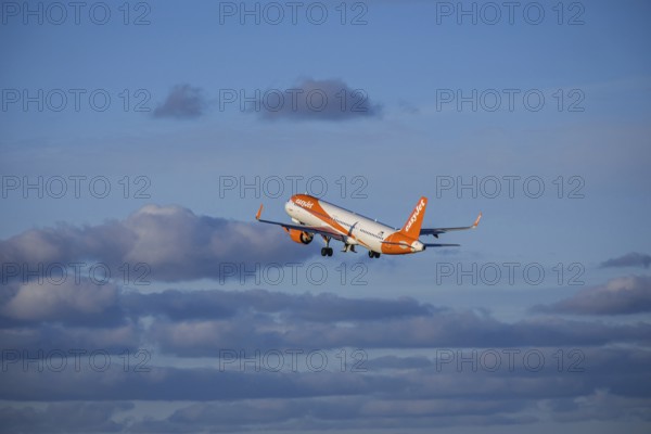 Lisbon, Portugal - Apr 29, 2024: EasyJet Airbus 321 neo aircraft shot mid-flight, ascending into clear blue sky with some clouds after takeoff on sunny day. Air traffic, vacations, travel, destinations, aircraft, low-cost airline, commercial flight