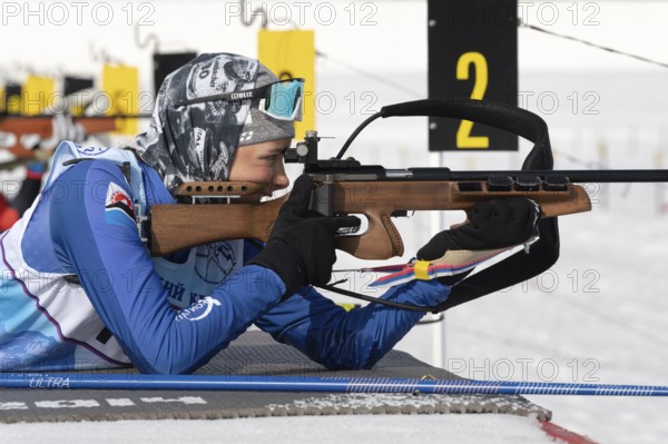 Sportswoman biathlete aiming, rifle shooting in prone position. Biathlete Arina Soldatova Kamchatka Peninsula in shooting range. Junior biathlon competitions East Cup. Kamchatka, Russia, Apr 13, 2019, Europe