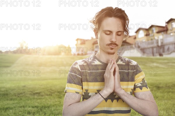Young man meditating outdoors in the park, sitting with eyes closed and his hands together. man praying to god