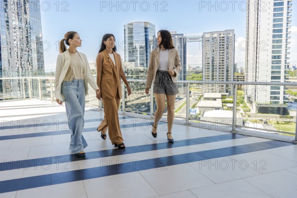 Three businesswomen are walking on a terrace of a tower building