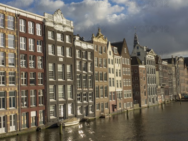 Row of historic canal houses on the waterfront with reflection and blue sky with clouds, amsterdam, the netherlands