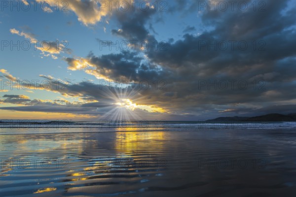 Sunrise over the ocean. Gentle cloud colors are reflected in the ocean water. Light wind causes small ripples in the water. The sun's rays make their way through the light morning clouds. Concept of artistic photography