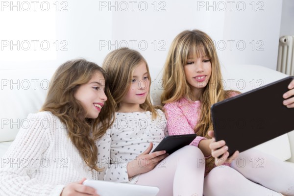 Three kid sister friends girls group playing together with tablet pc on white sofa