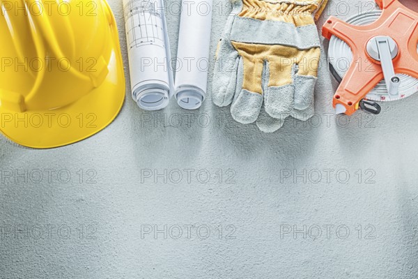 Safety gloves hard hats blueprints measuring tape on concrete background