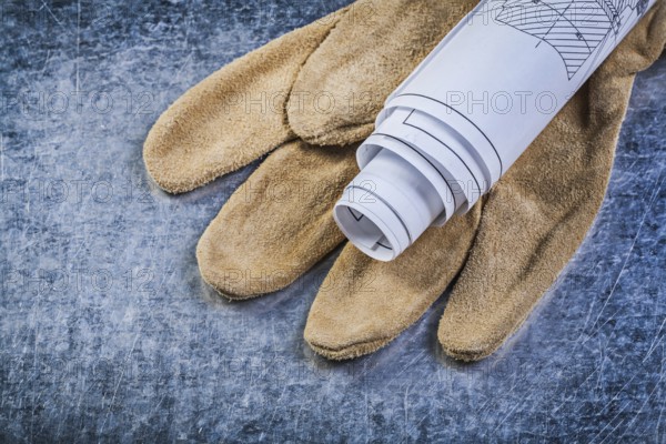 Rolled up engineering drawings leather protective gloves on metallic background construction concept
