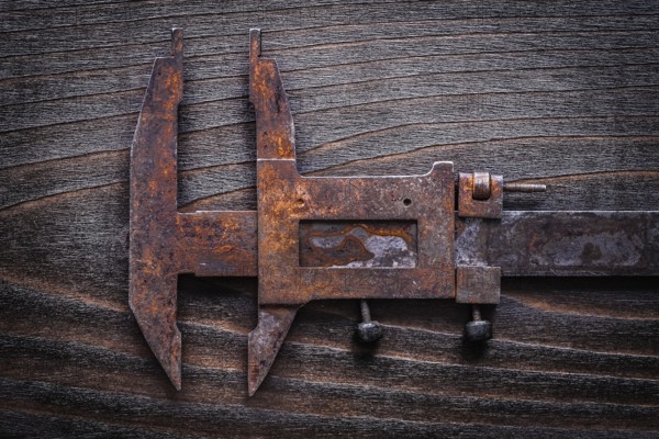 Rusted old-fashioned measuring slide caliper on vintage wooden board construction concept