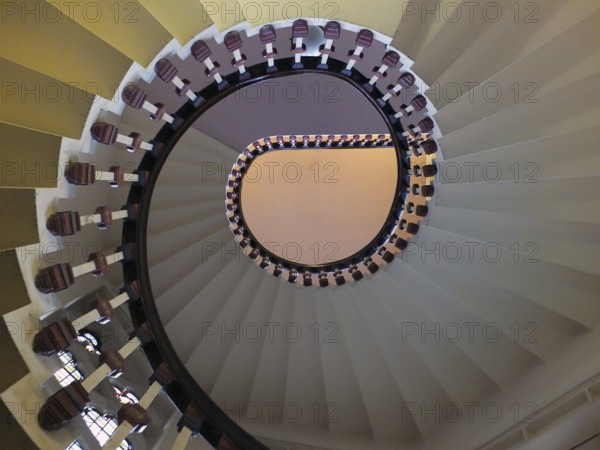 A looking upwards view of an elegant spiral staircase with wooden bannisters in elegant shades of white