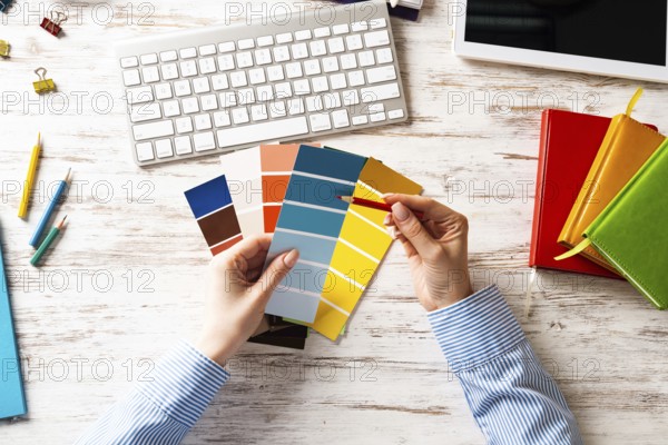 Interior designer choosing colors from swatches at wooden desk. Office workplace with computer keyboard. Selection of color palette for design. Professional house renovation and interior redesign
