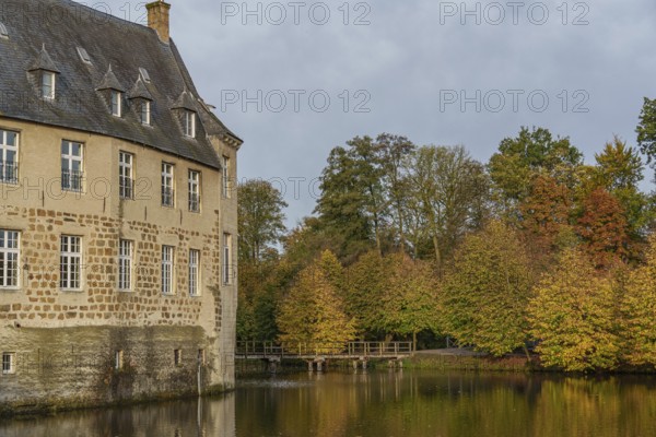 Historic castle on the shore of a lake with colourful autumn trees in the background, Borken, Münsterland, Germany, Europe