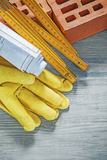 Composition of red bricks protective gloves blueprints wooden meter on wood board bricklaying concept