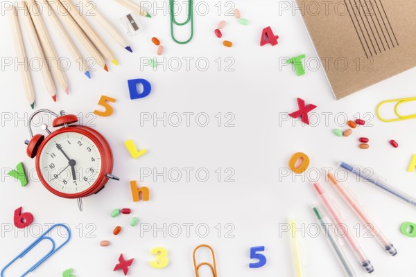 Creative flat lay back to school concept with alarm clock, color school and office supplies on white table background with copy space, frame, template for text or design