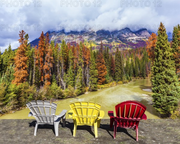 Scenic autumn in the Rockies of Canada. Three deck chairs stand over the forest and river. Thunderclouds swirl in the sky. Concept of ecological, active and photo-tourism