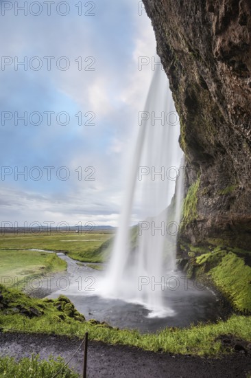 Sunny day in Iceland. Seljalandsfoss waterfall in July. Large rainbow decorates a drop of water. Passage under the waterfall