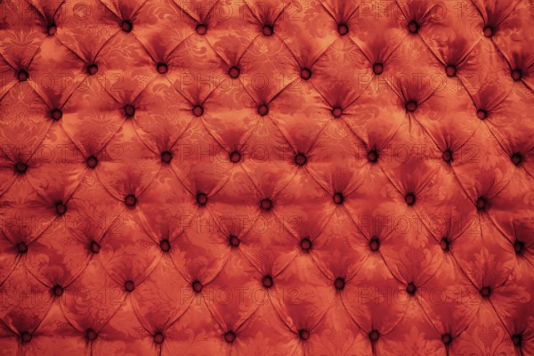 Close up background texture of scarlet red capitone genuine leather, retro Chesterfield style soft tufted furniture upholstery with deep diamond pattern and buttons.