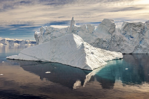 Large iceberg with striking reflection in calm water, surrounded by clouds and blue sky, icebergs in the landscape of the Southern Ocean in Antarctica