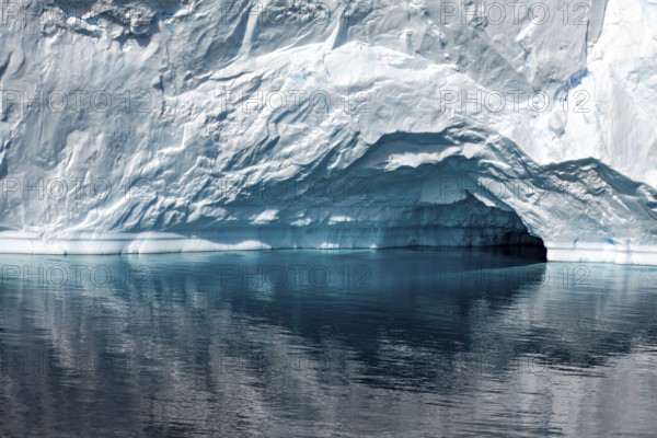 A large iceberg with a small cave is reflected in the calm, reflective water, icebergs in the landscape of the Southern Ocean in Antarctica