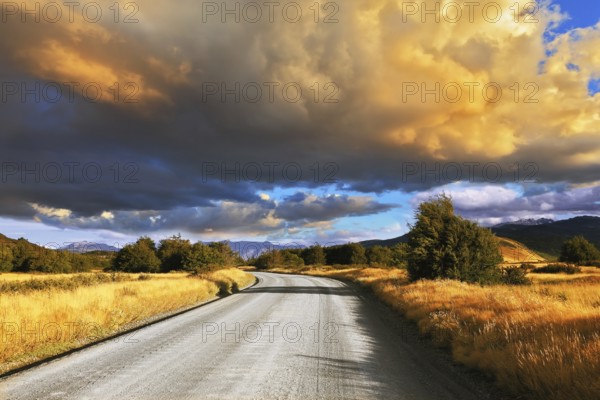 The huge cloud lit yellow-orange rays of sunset. Gravel road through the Patagonian steppe
