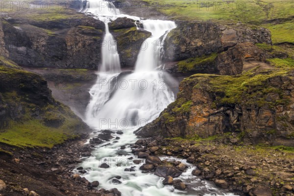 Powerful streams of cascade falls with a roar break against cold rocks. Cold and rainy July in Iceland