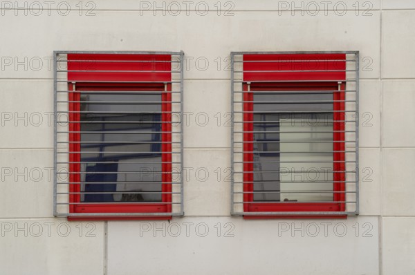 Two windows with red frames and metal grilles restrict the view outside