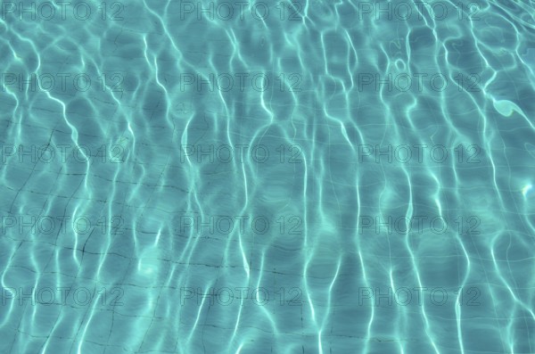 Waves on the light of the pool water. Swimming pool with blue water. Water surface texture. View from above.