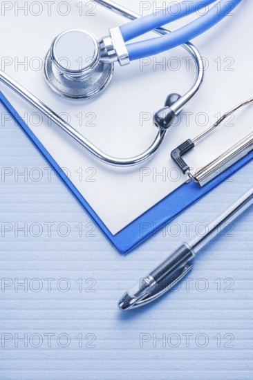 Ballpoint pen and stetoscope with clipboard on blue background medical concept