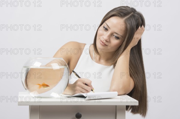 A young girl sits next to a round aquarium in which swimming goldfish
