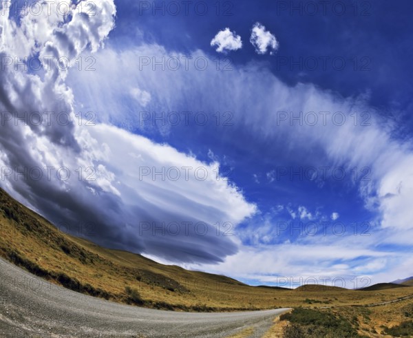 Gray dirt road in the Chilean national park to Torres del Paine. Improbable form the clouds created by glaciers, shine under the sun. On the horizon mountains with snow tops are visible. The photo is made a lens the Fish eye