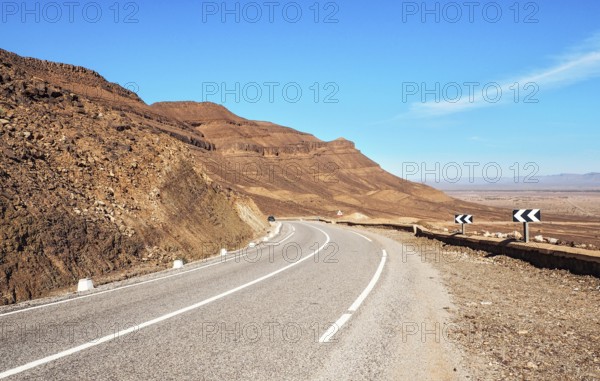 Kurve auf Asphaltstraße, kleine Atlas Berge und niedrige Büsche beide Seiten, klare Himmel über - typische Landschaft im Süden Marokkos