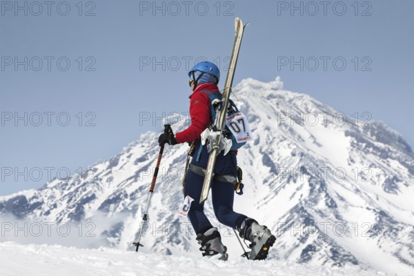 AVACHA VOLCANO, KAMCHATKA, RUSSIA, APR 21, 2012: Open Cup of Russia on ski-mountaineering. Girl ski mountaineer climbing on mountain with skis strapped to backpack on background active Koryak Volcano