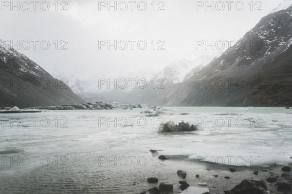 Mountain valley with frozen lake, surrounded by snow-capped mountains under a cloudy sky, Hooker Valley Track, New Zealand, Oceania
