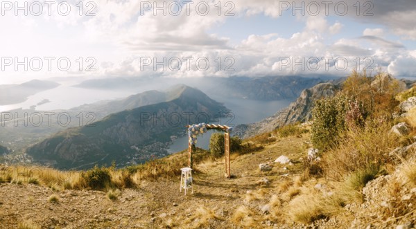 Simple wooden arch decorated with flowers stands on top of a mountain overlooking the valley.